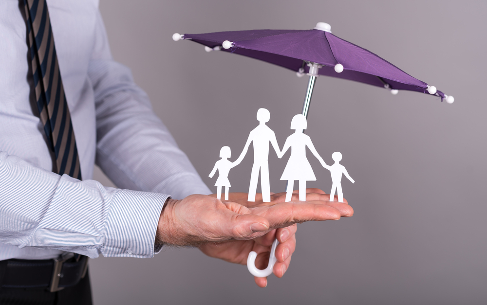 man with hand out and umbrella over family cutouts signifying umbrella insurance