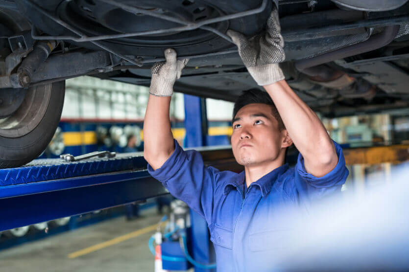 Man in blue shirt wirth raised hands standing under a car while he is giving it car maintenance in auto garage