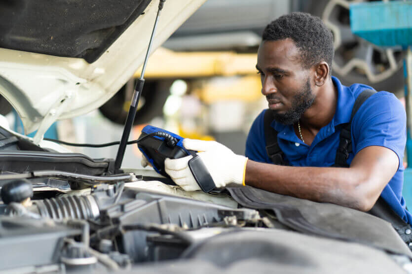 Man in blue shirt standing by car with hood up checking to find cosmetic car issues such as dents and ding