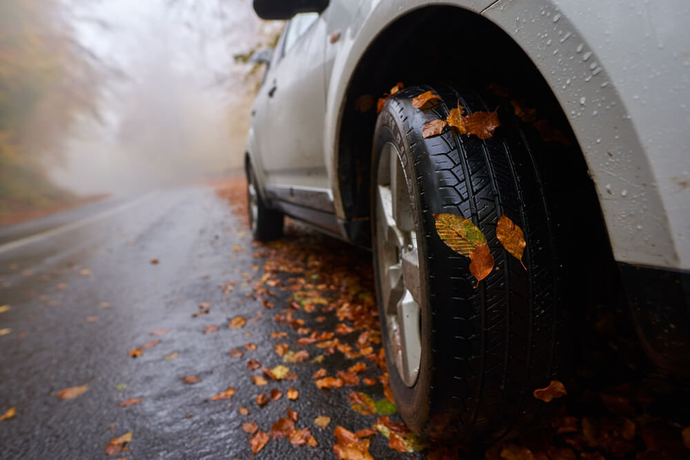 Closeup of a car with leaves stuck on wheels on a wet road in the autumn, concept of driving safely in fall in rain and leaves, good car insurance.