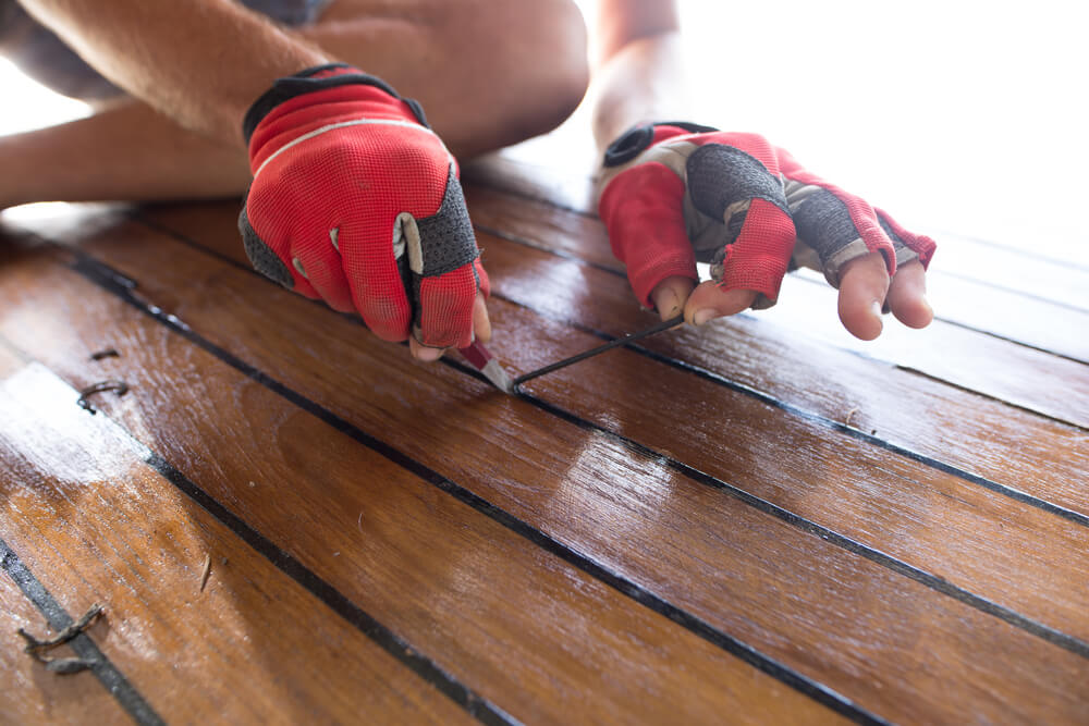 Hands prepare the wood on a sailboat deck prior to going out for spring.