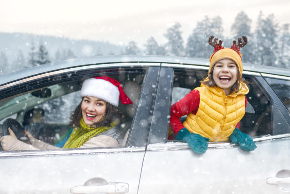 Woman and young girl looking out car windows and laughing as snow falls.