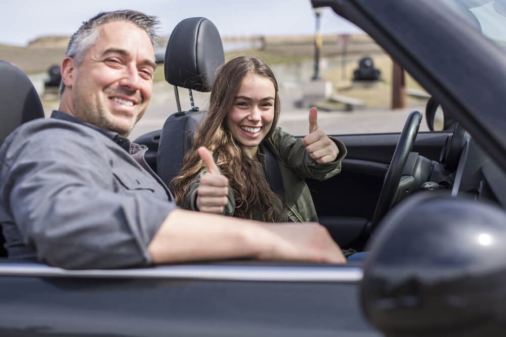 Father and daughter sitting in car giving thumbs up, father teaching his daughter to drive in the family convertible - best car insurance.