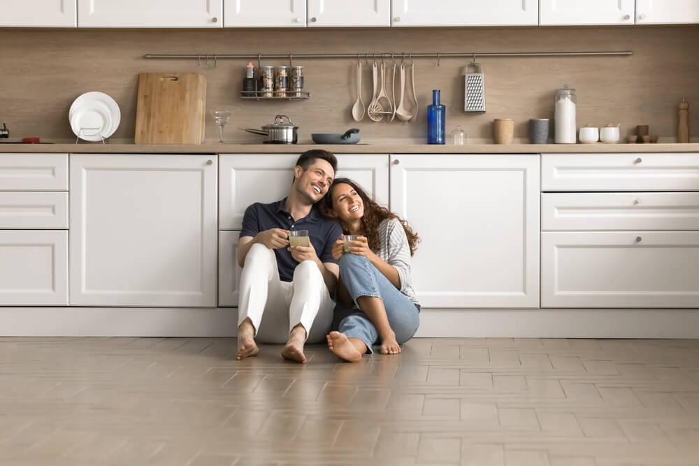 Happy couple sitting on kitchen flow drinking tea looking out a window.
