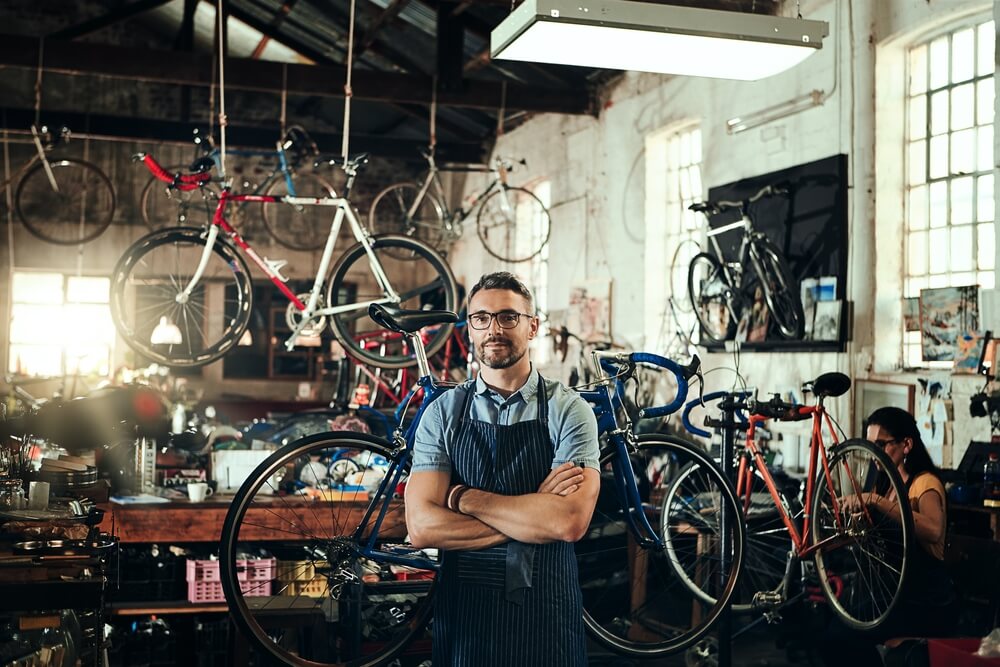 Bicycle shop owner stands with his arms crossed in front of bicycles - best business insurance.