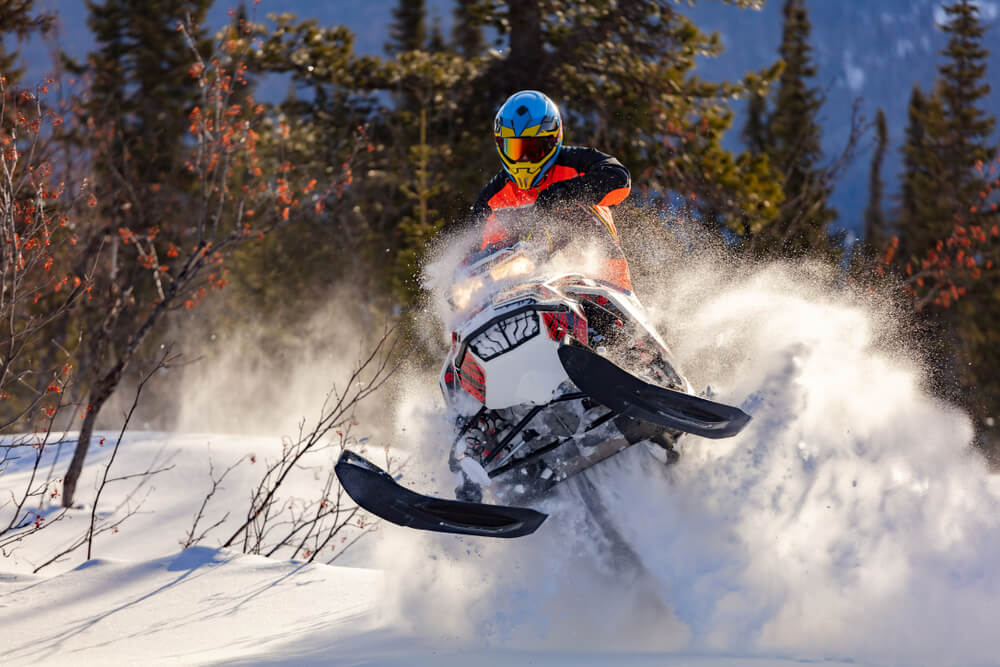 Person on a snowmobile kicking up the snow on a mountain trail - best snowmobile insurance.