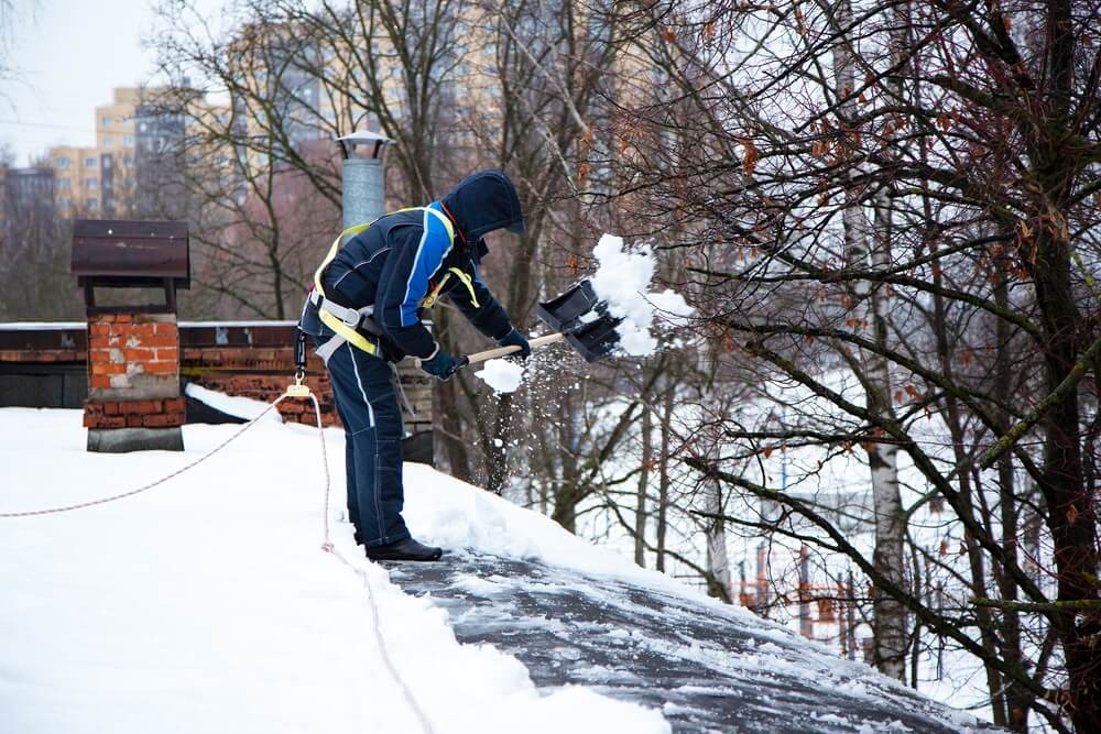 Professional shovels snow off the roof of a home - best homeowners insurance.