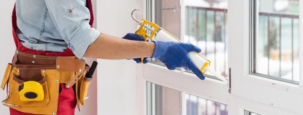 Man seals windows against the cold with caulk - best homeowners insurance.