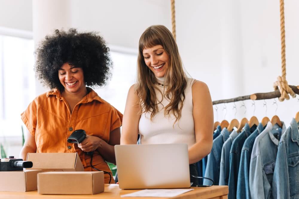 Two smiling female workers in clothing shop, happy to have workers comp benefits.