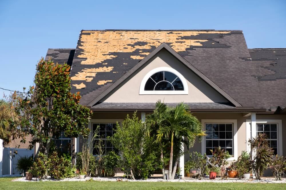Wind damaged house roof with missing asphalt shingles after hurricane Ian in Florida