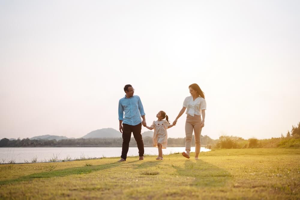 Mother and father with child walking in park next to water - best life insurance.