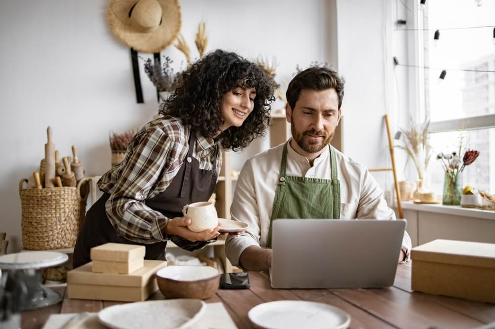 Two small business owners working together on a laptop in their shop, discussing strategies for business insurance growth as their business develops.