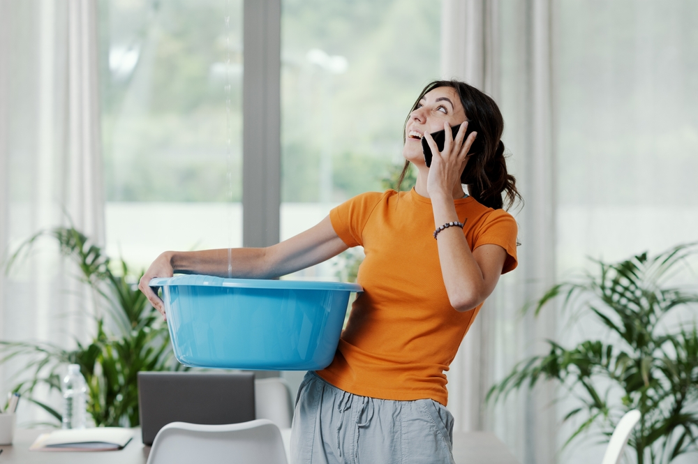 Aggravated woman on phone and holding bucket to catch water coming in through the roof - best home insurance