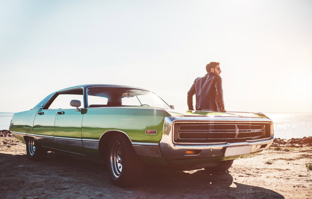 Man is standing near his green retro car on the beach - Best Auto Insurance