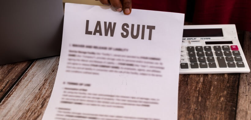 A hand holding a lawsuit document with peace of mind thanks to business lawsuit protection, next to a calculator.