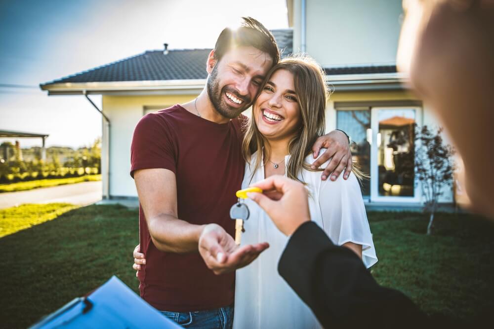 Landlord hands the keys to a rental home to a young couple who are smiling.
