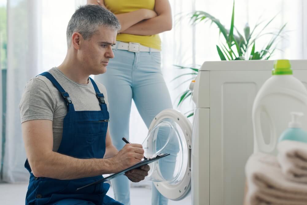 Repairman examines non-working appliance under home warranty while homeowner looks on from behind - best home insurance.