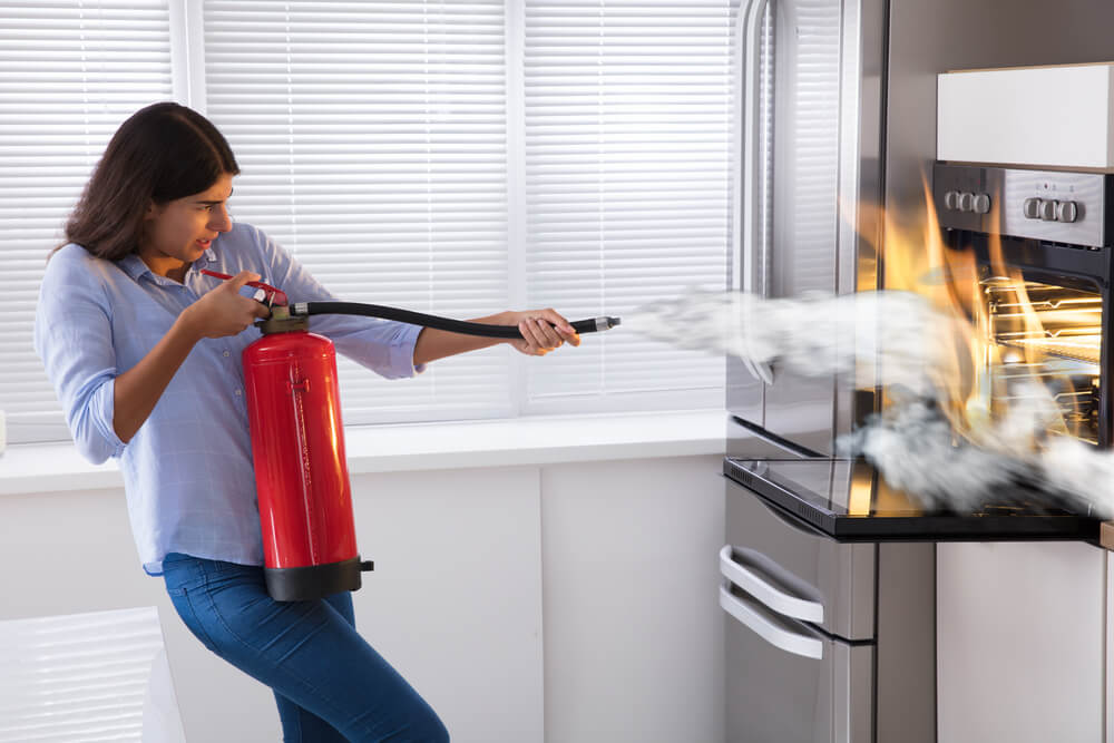 Young woman using fire extinguisher to put out fire from oven at home, home insurance and fires.
