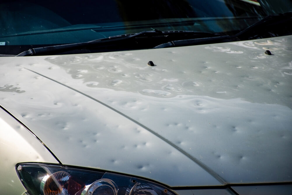 A car with its hood dented from hail - best car insurance.
