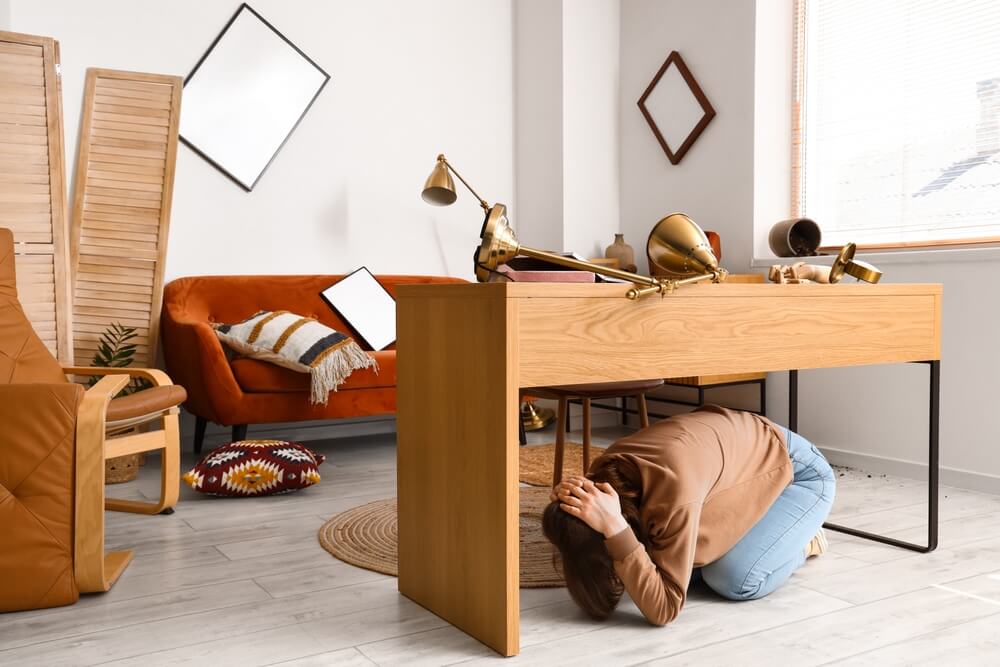Woman protects herself under a desk at home during an earthquake.