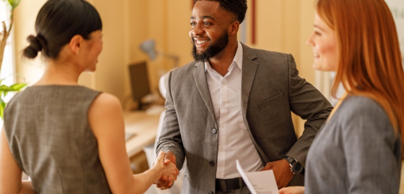 Male entrepreneur smiling and shaking hands with female partners in a modern workspace, representing a business protected by insurance-1