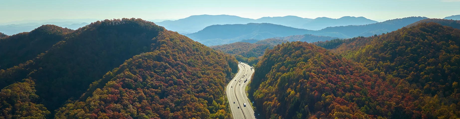 View from above of I-40 freeway in North Carolina heading to Asheville through Appalachian mountains in golden fall season with fast driving trucks and cars. Interstate transportation concept