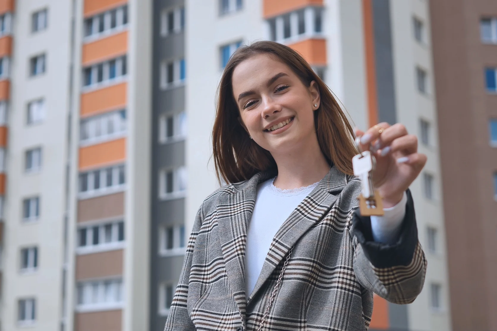 The girl shows the keys to the apartment against the backdrop of an apartment building – best habitational insurance.
