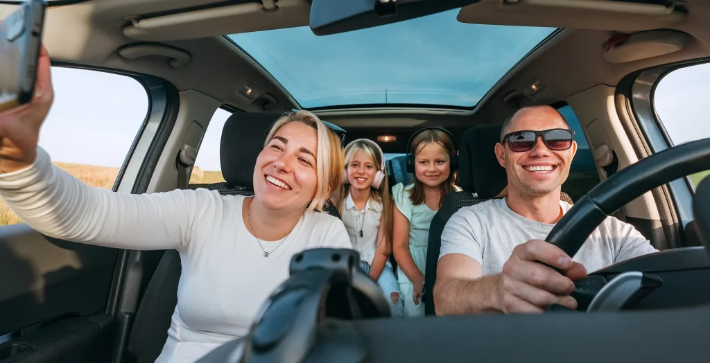 Two trendy attractive young woman singing along to the music as they drive along in the car through town viewed through the open side window, happy for the best car insurance with bundled discount.